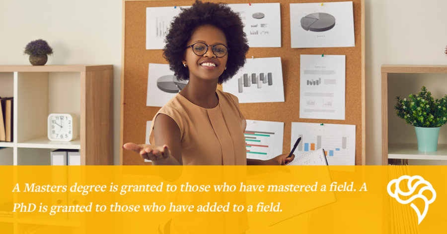 A person stands in front of a corkboard full of printed graphs, smiling and pointing at one